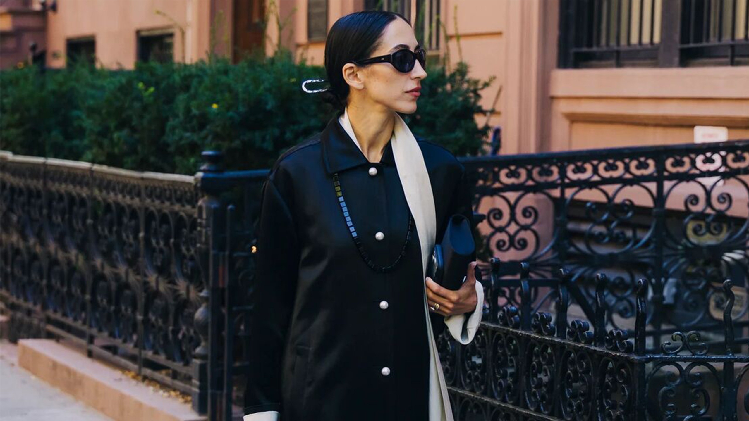 Woman wearing a buttoned-up black coat and a long beaded necklace.