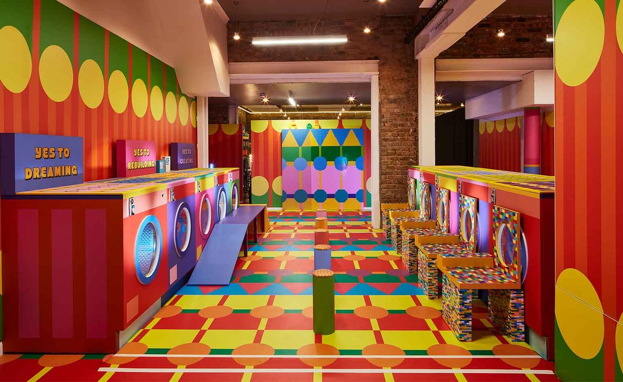 Interior view of Yinka Ilori&#039;s Launderette installation featuring mock washing machines in bright colours