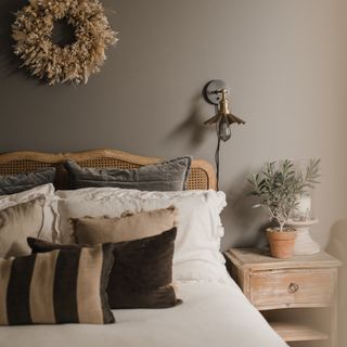 bedroom wall decor, taupe bedroom with wood and rattan bed, textured cushions, dried wreath on wall and metal wall lamp, weathered wood side table