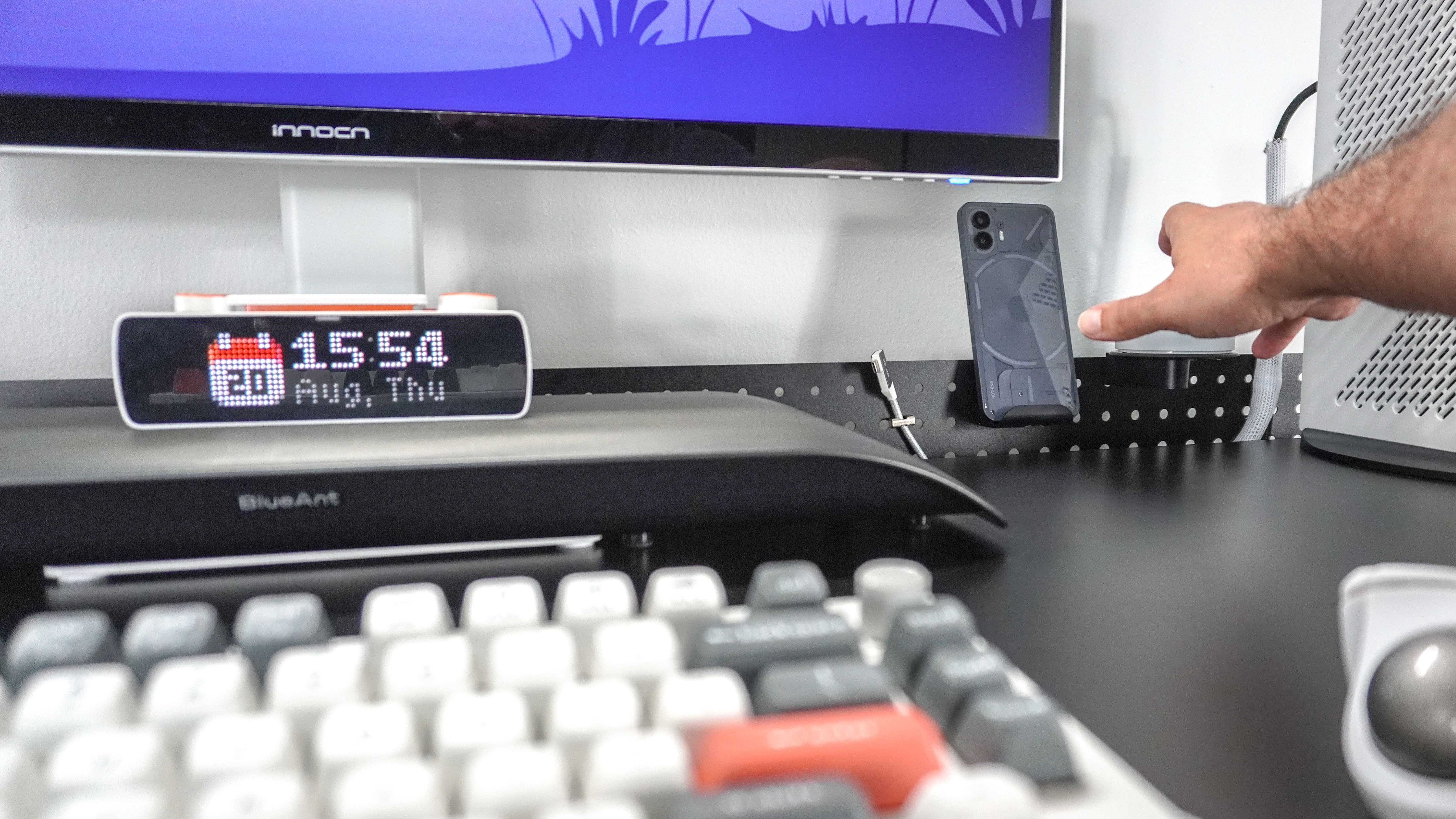 A person reaching across the Herman Miller Coyl Gaming Desk to get their phone from the optional stand installed on the shroud at the back of the desk