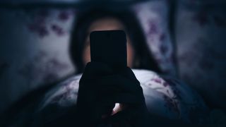 Woman in bed holding a phone in front of her, with the light from the screen illuminating her face