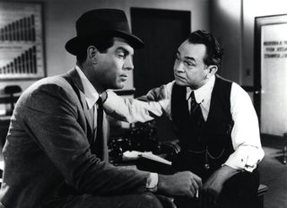 one man puts a hand on another man's shoulder in an office in the movie Double Indemnity