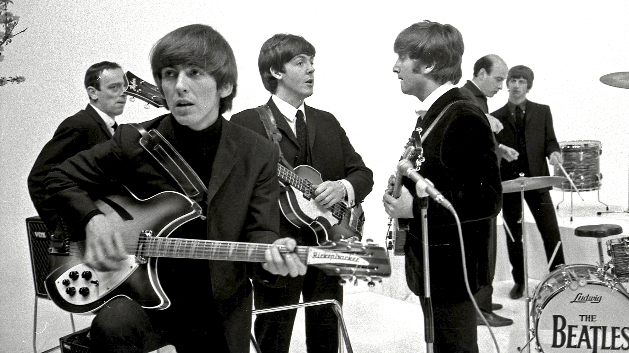 The Beatles on the set of A Hard Day's Night. L-R: John Junkin, George Harrison (playing Rickenbacker 360/12 guitar), Paul McCartney, John Lennon, Richard Lester (director), Ringo Starr during the filming of 