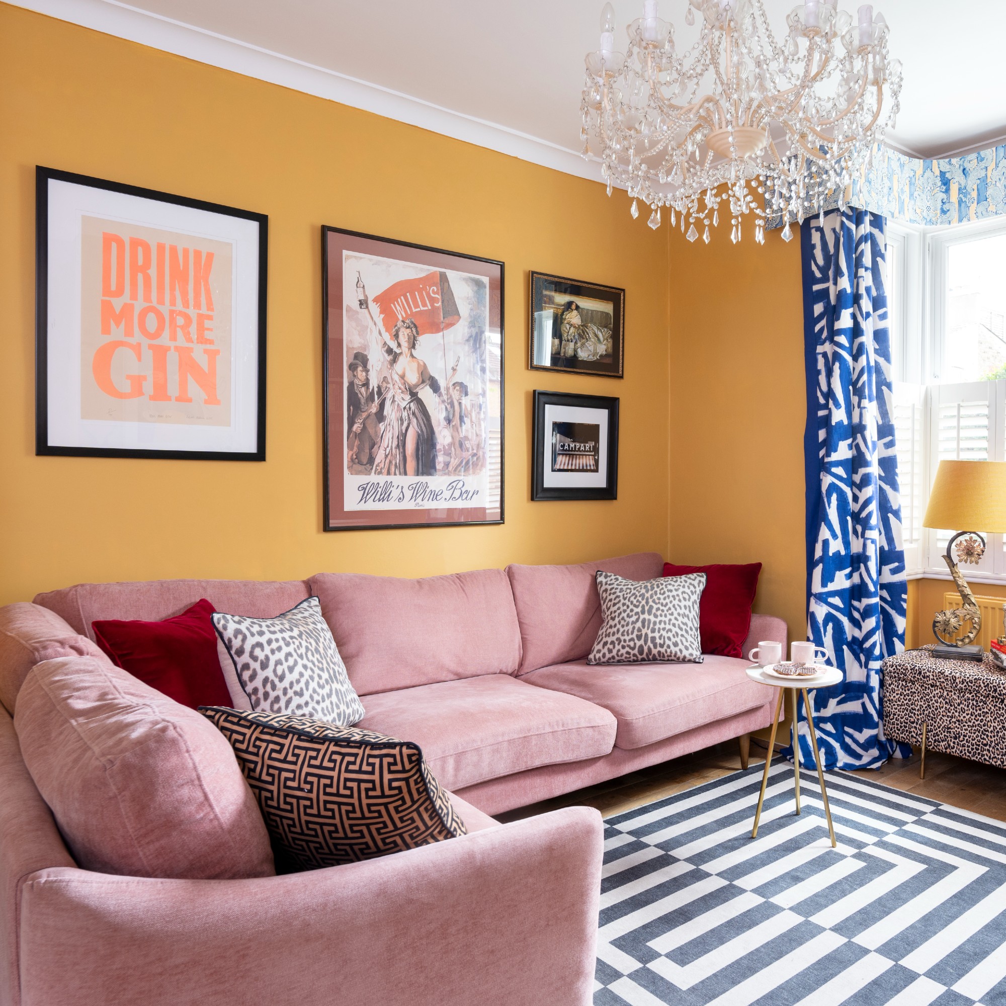 A yellow living room with a pink velvet corner sofa and a rectangular geometric-print rug