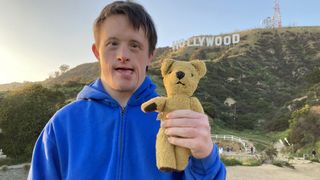 Tommy Jessop in a blue jumper holding his teddy Roger in front of the Hollywood sign in Tommy Jessop Goes to Hollywood.