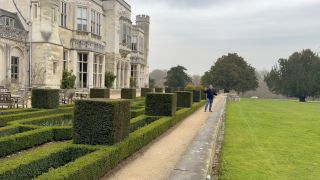 A presenter talks to camera in front of a British stately home