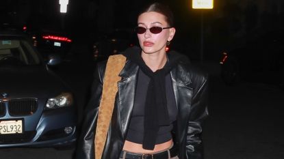Hailey Bieber in a church outfit of a black crop top, suede pants, leather trench