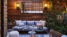 Wood-clad outdoor terrace with evening lighting, comfy sofa and side tables with candles and glasses of wine