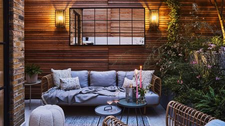 Wood-clad outdoor terrace with evening lighting, comfy sofa and side tables with candles and glasses of wine