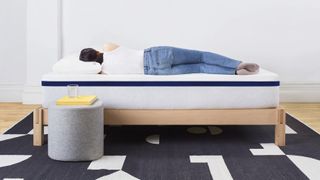 A woman wearing a white vest and blue jeans sleeps on her side on the Helix Midnight Mattress