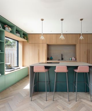 kitchen with wood cabinetry, waterfall island with bar stools, green bookshelf, pendants, herringbone floor,