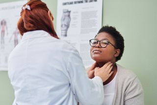 A doctor examining a patient's throat by feeling either side of the neck just under the chin.