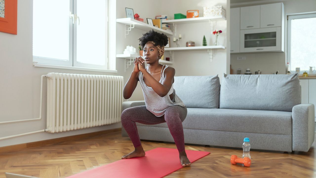 woman performing a bodyweight squat on a pink mat in a living room setting