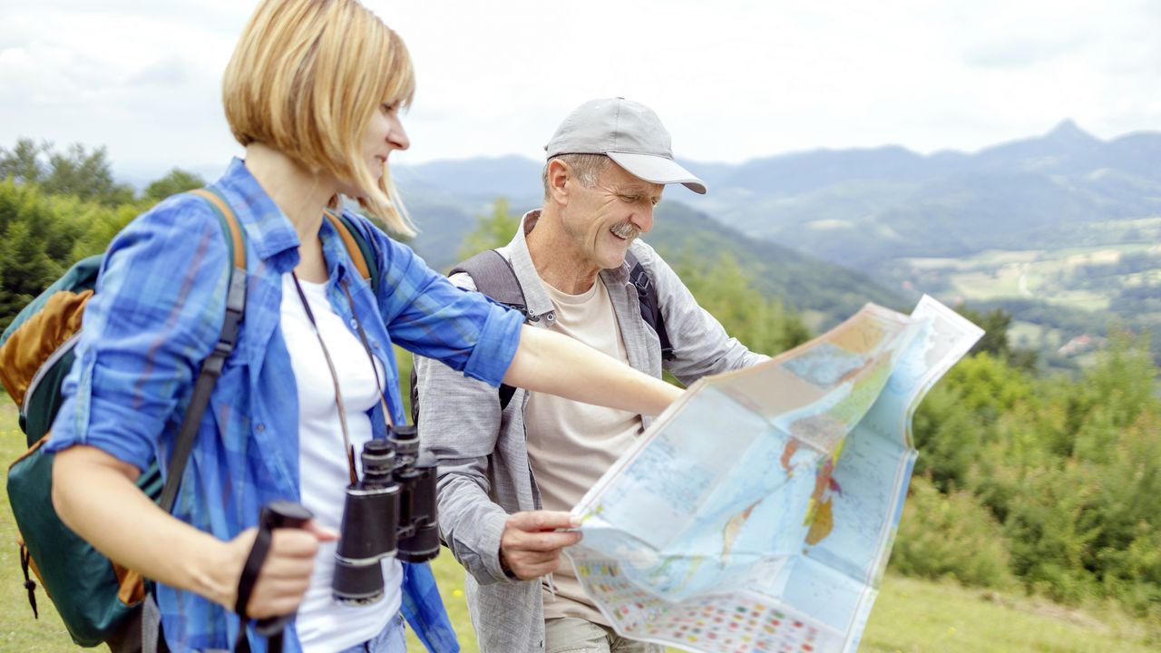 A daughter and her father look at a map while hiking on a mountain.