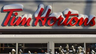 Photo of a large, red Tim Hortons sign on a storefront, topped with recently fallen snow