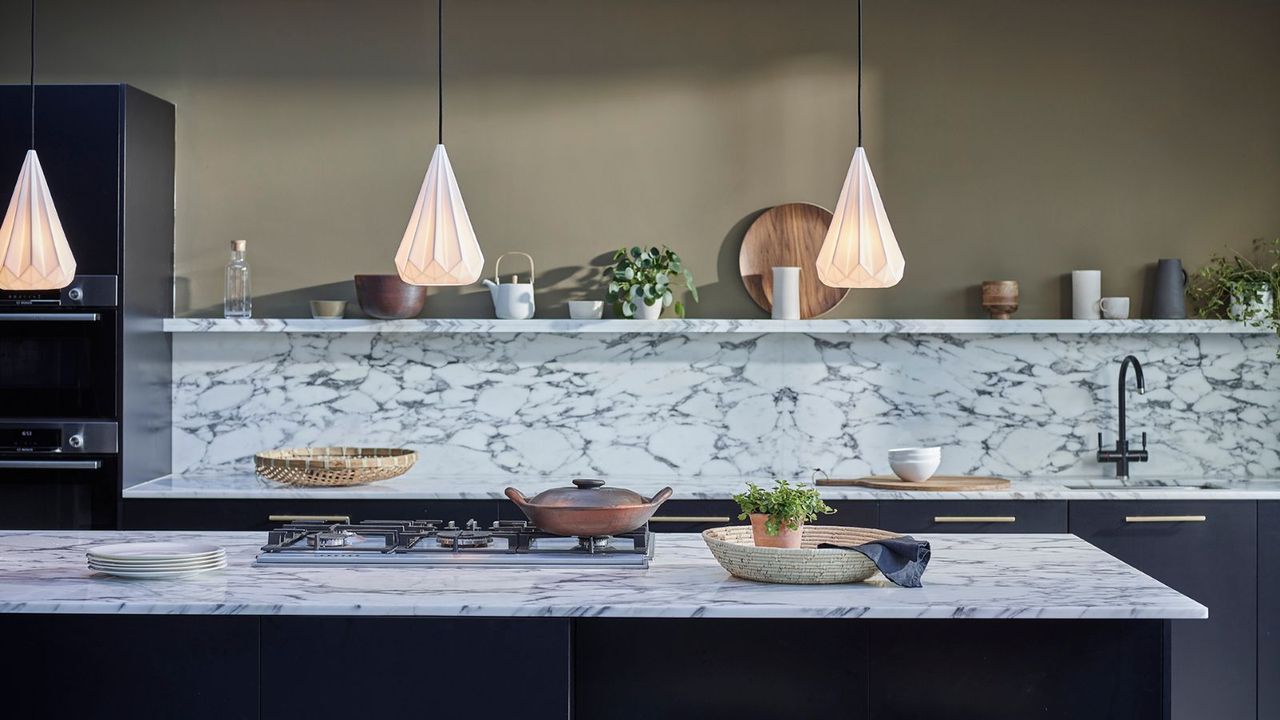 A kitchen with white marble backsplash and open shelf, a kitchen island with low hanging pendants 