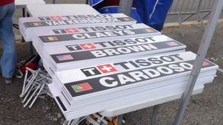 Each rider has a dedicated team car following them, marked with their name ahead of the start