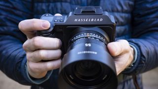 Hasselblad X2D 100C camera in user's hand, their blue jacket in background