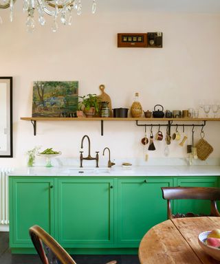 A kitchen with green lower cabinets, neutral walls, and wooden open shelving