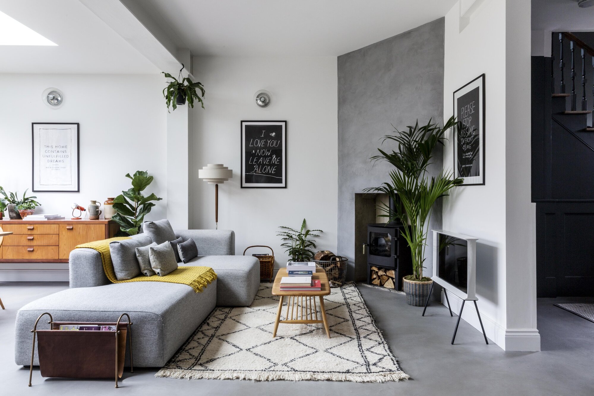 modern living room with polished concrete floors, boho rug, gray boxy sofa with cushions and yellow throw, magazine rack, and mid-century style furnishings