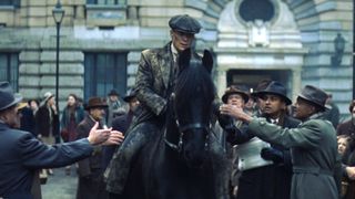 Tommy Shelby (Cillian Murphy) rides a black horse through a city street as a crowd gathers around him