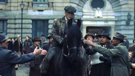 Tommy Shelby (Cillian Murphy) rides a black horse through a city street as a crowd gathers around him