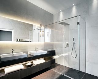 Modern, minimalist bathroom with sleek shelving and modern vanity unit, shelves and mirrors lit up with LED lighting, large shower space, textured gray wall tiles, dark gray floor tiles