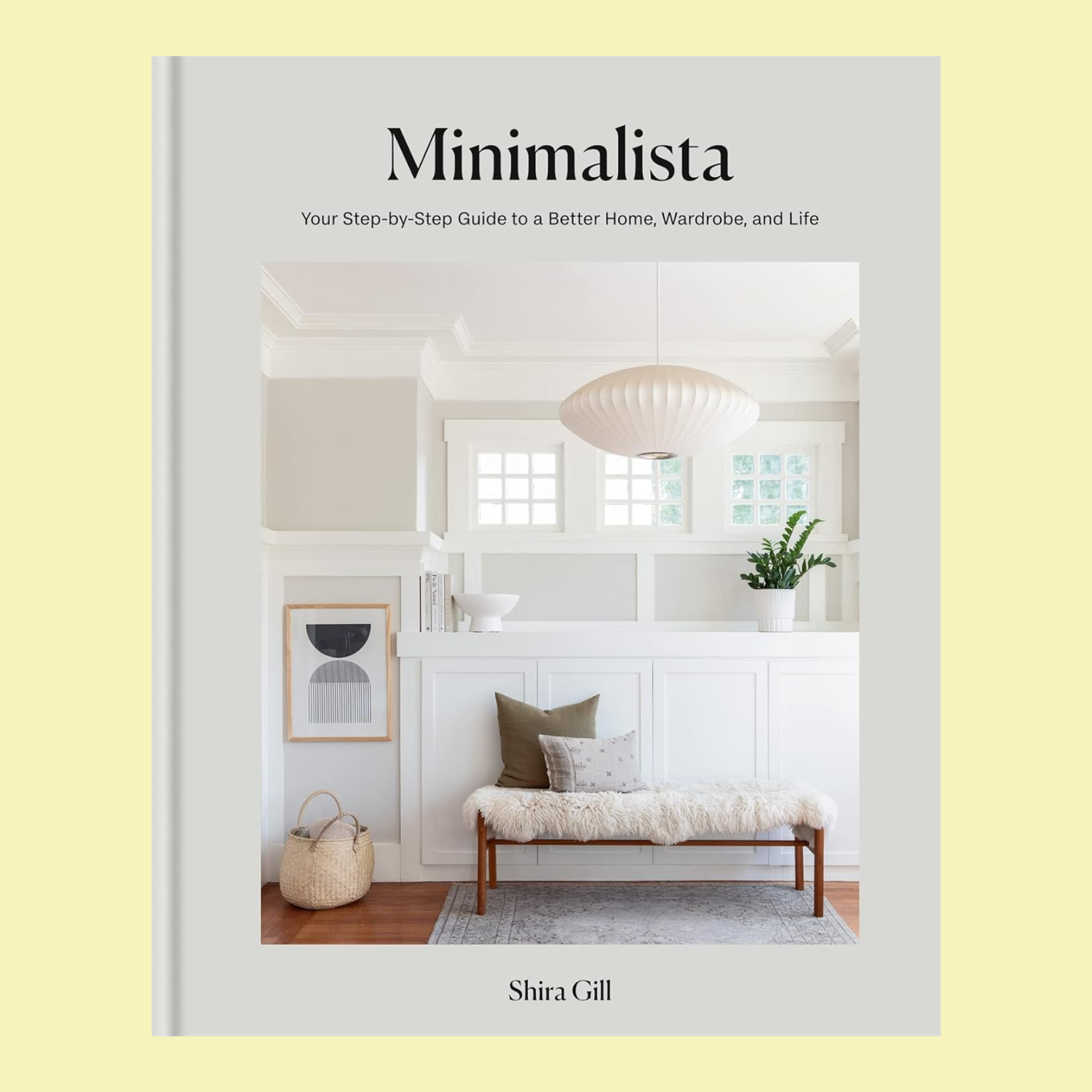 A hardcover book with a snapshot of a minimalist entryway, titled 'Minimalista: Your step-by-step guide to a better home, wardrobe and life' by Shira Gill