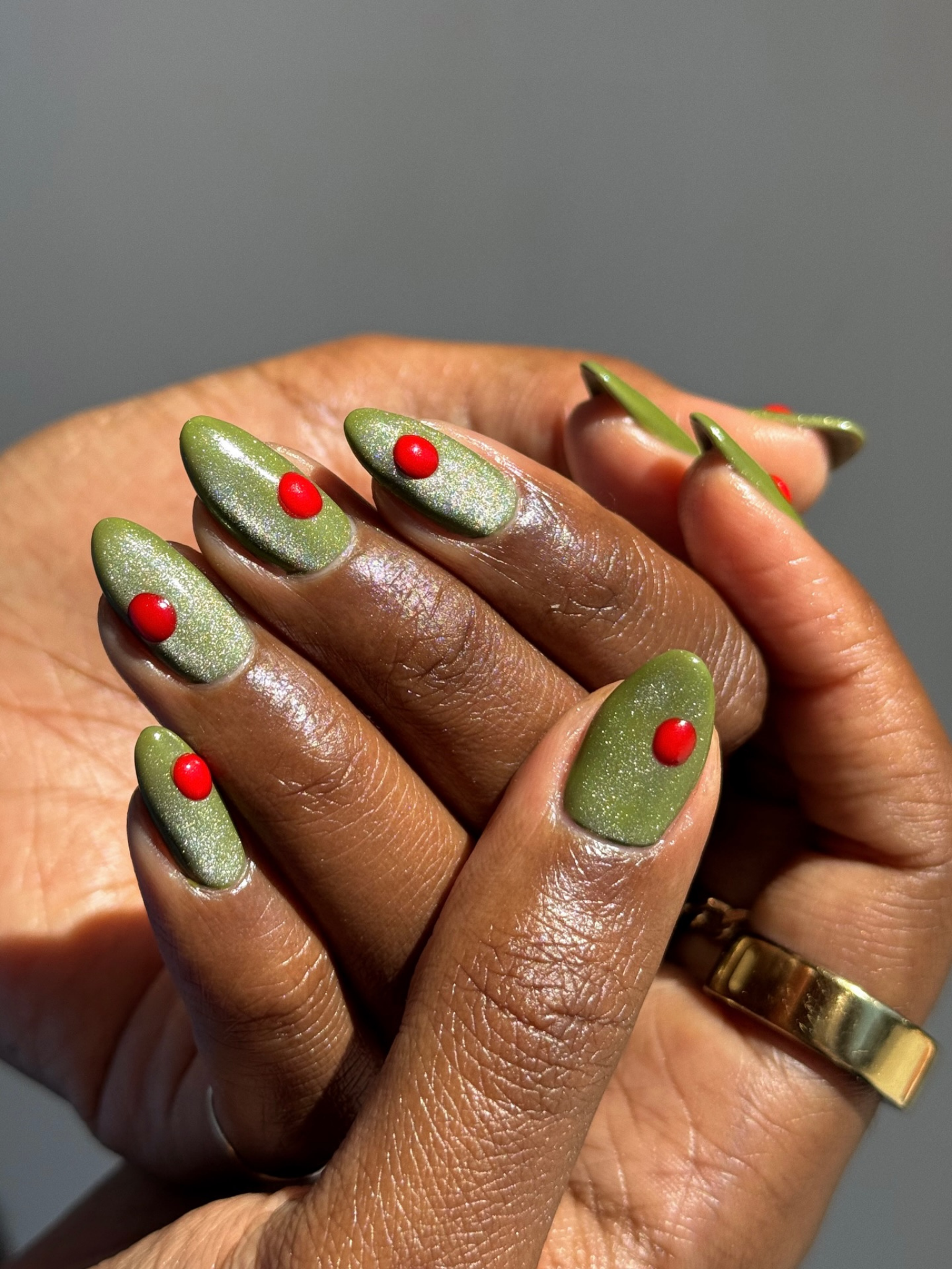 Khaki green nails in a shimmer finish with a red dot detail on each nail