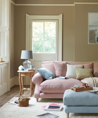 living room with beige walls, a soft pink sofa and a baby blue footstool and accessories