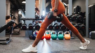 Woman performs split squat with dumbbells in gym