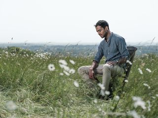 An individual say on a chait in the middle of a green field in the sunlight