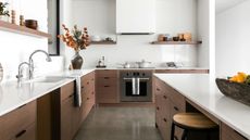 A kitchen with quartz countertops and a large island in the middle. Beside the island is one bar stool and on the other side of the countertop are double taps with a sink. On the worktops are several kitchen accessories as well as a flower inside a vase