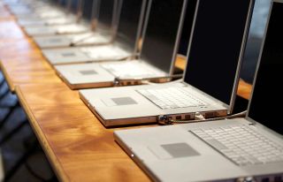 A row of open laptops computers fades into the distance on school tables