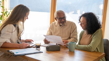 An older couple look happy as they look at paperwork with their financial adviser.