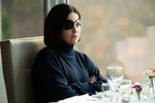 Sarah Greene as Bibi Harvey, wearing a black eye patch and sitting with her arms crossed at a dining table, in 'Bad Sisters.'