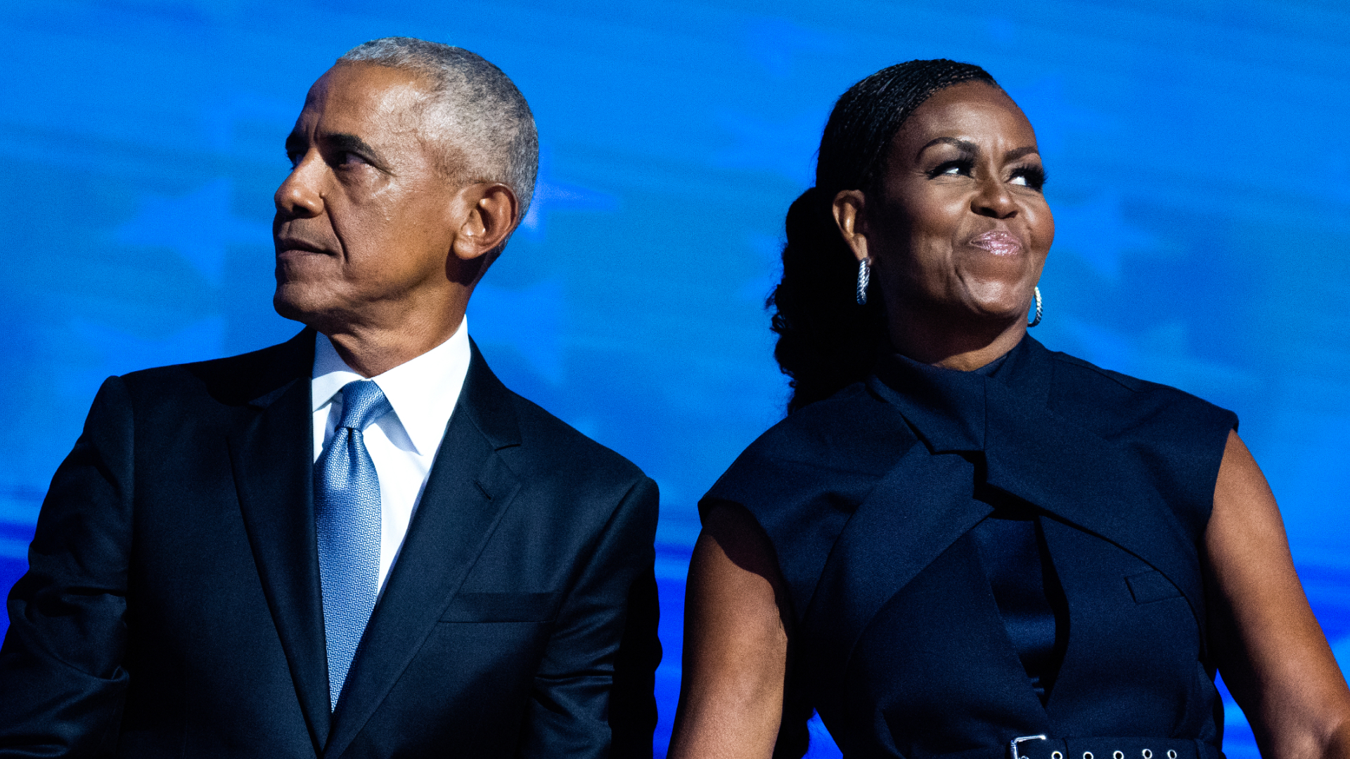Barack Obama and Michelle Obama hold hands while moving in different directions onstage