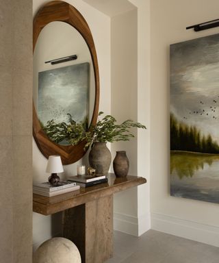 Neutral hallway with large wooden mirror, stone entry table, stone vases and books