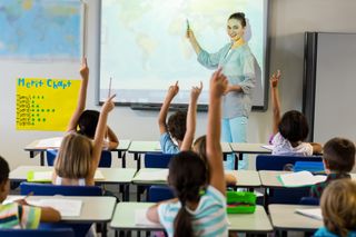 Teacher standing before class pointing to projector screen.