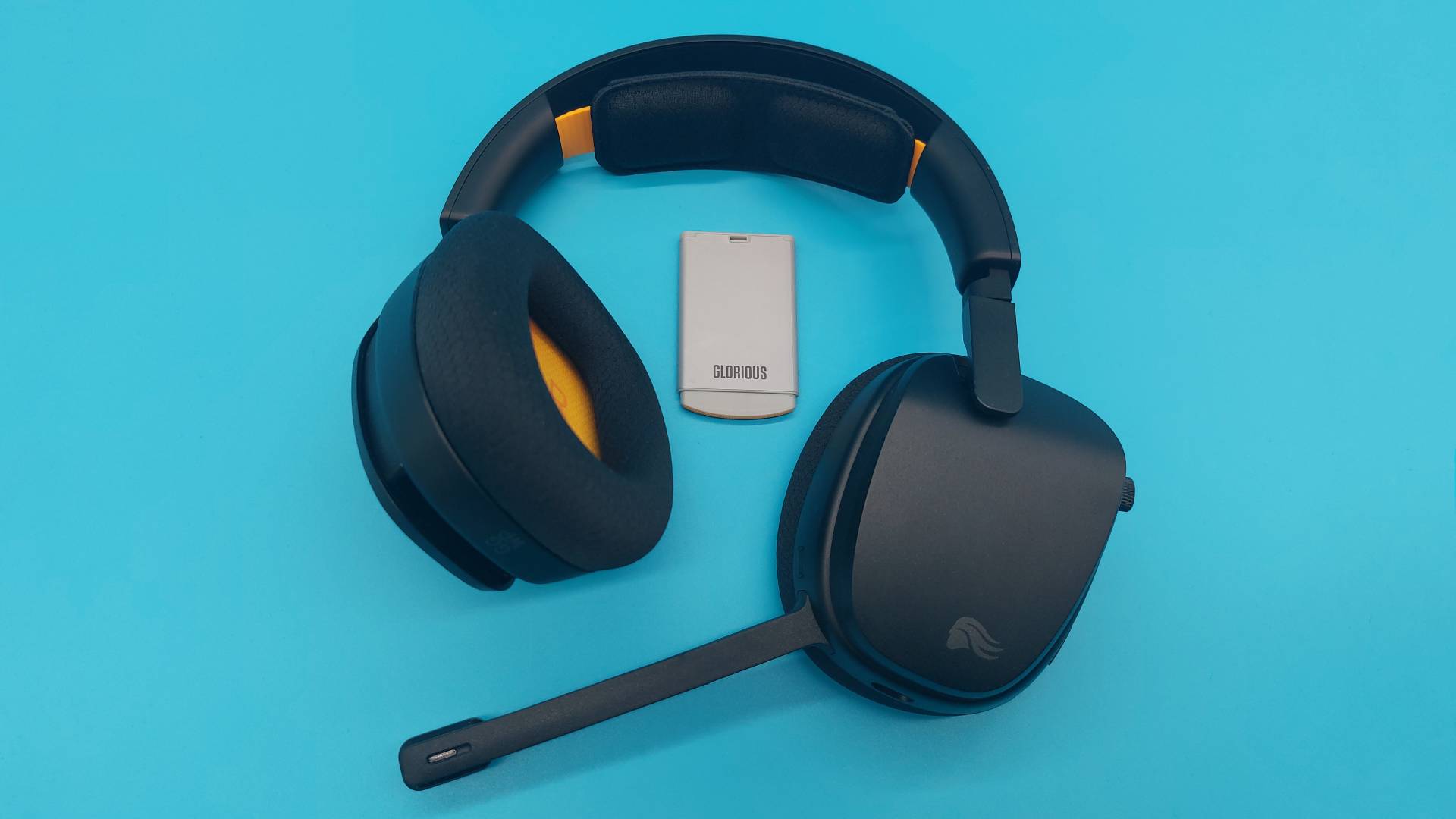 The GHS Wireless InfinitePlay seen from various angles on a blue background. This is a wireless gaming headset from Glorious. It is black all over, save for a few subtle orange accents.