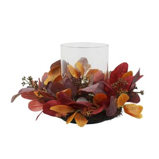 A fall candle holder with dark brown and purple leaves and a glass candle holder in the middle