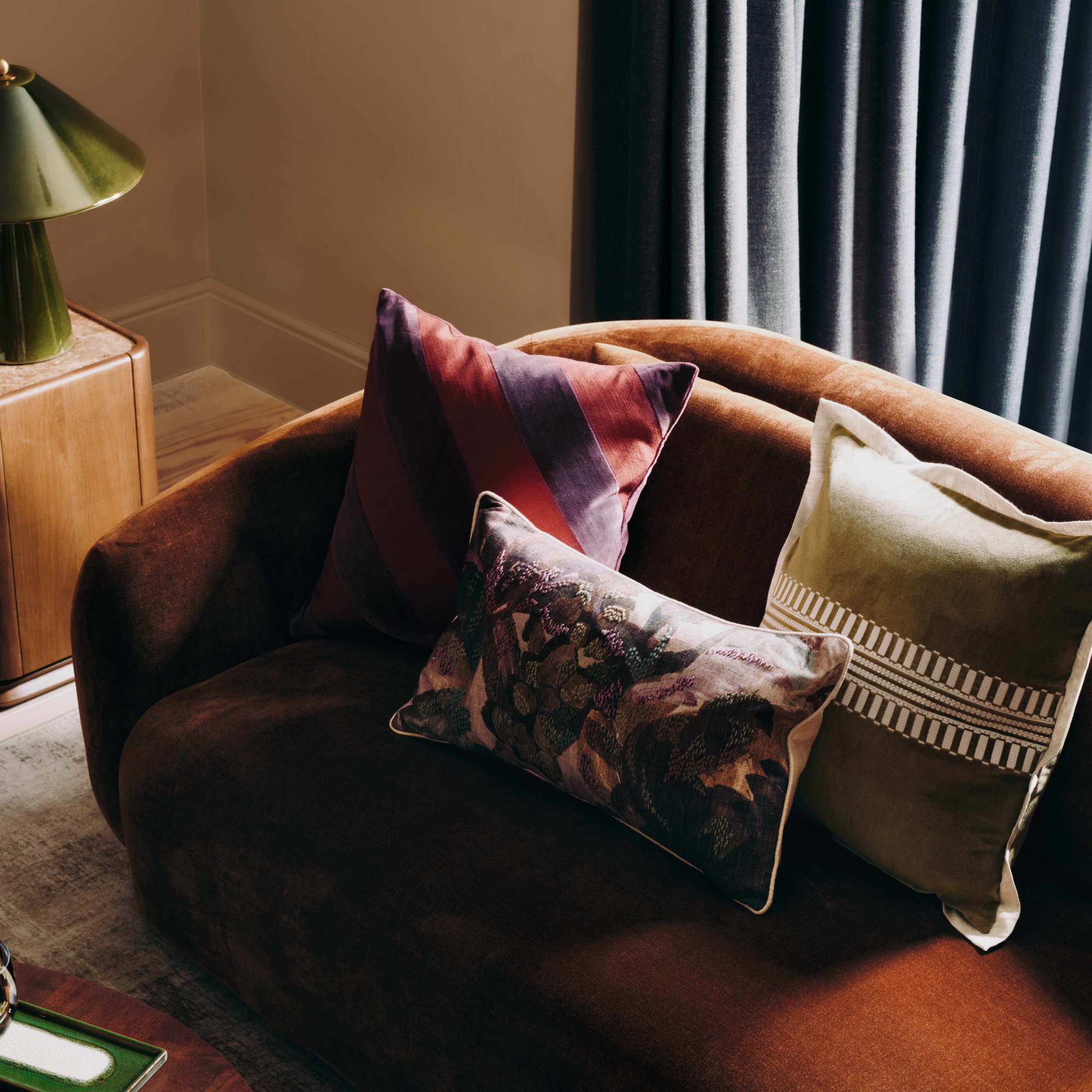M&S All Over Ceramic Table Lamp in green on a dark wood side table next to a brown velvet sofa with patterned cushions