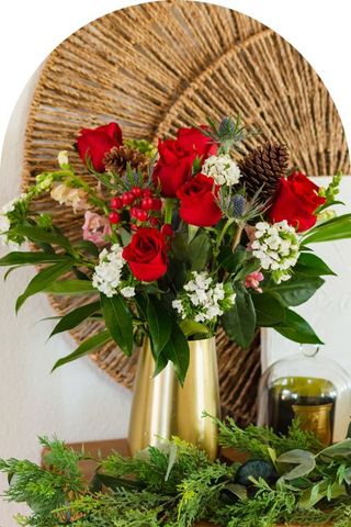 A bouquet of red and white flowers with pinecones and greenery, in a gold vase.
