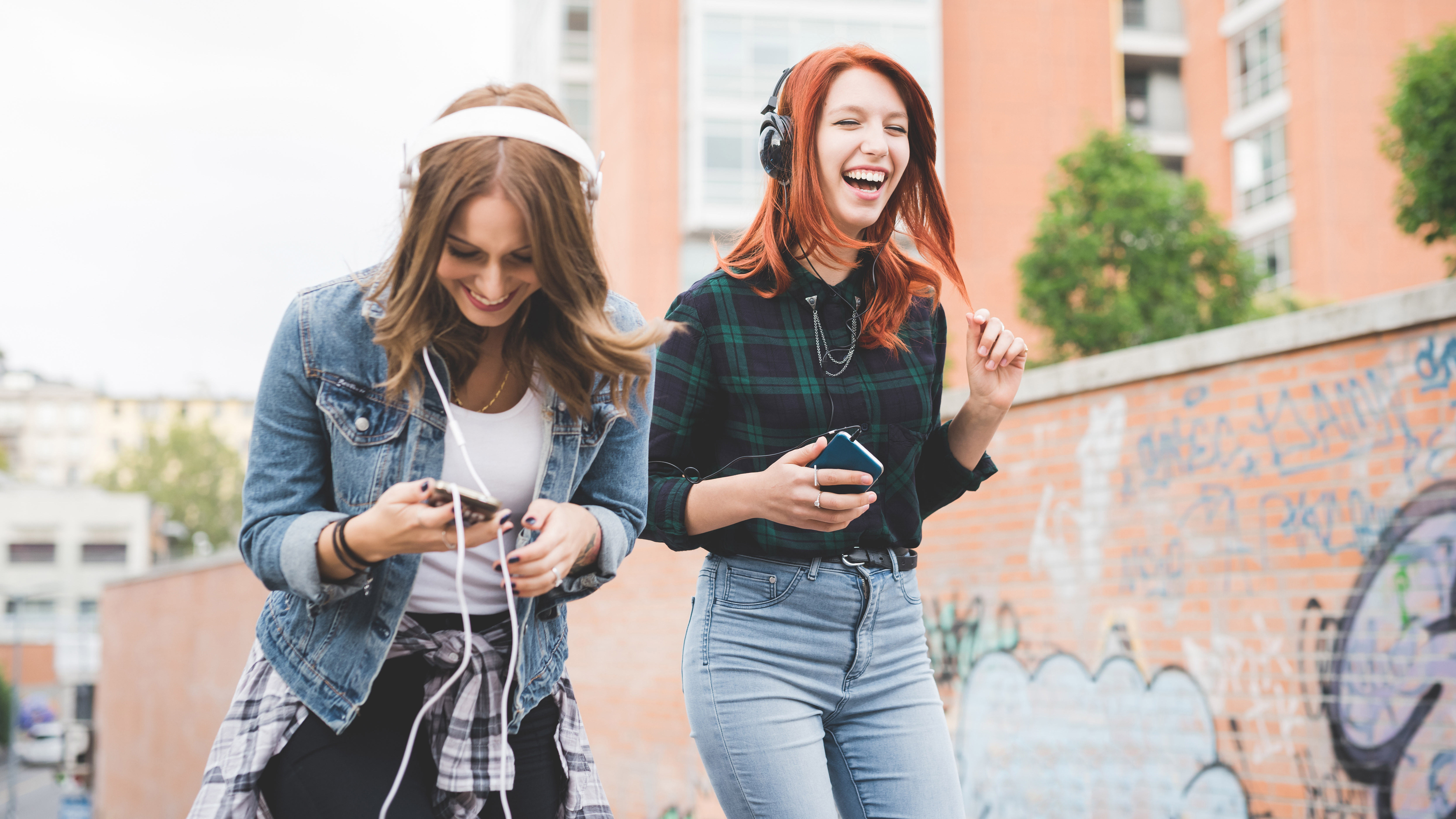 Two young women dancing in the city listening to music with headphones