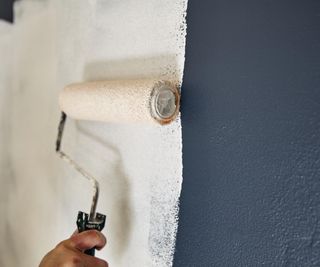 painting over a dark wall with white paint using a roller