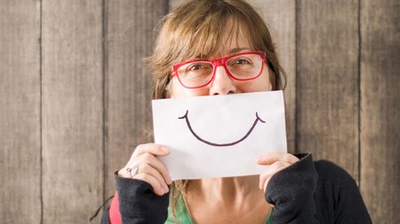 A woman holds a drawing of a smile in front of her mouth