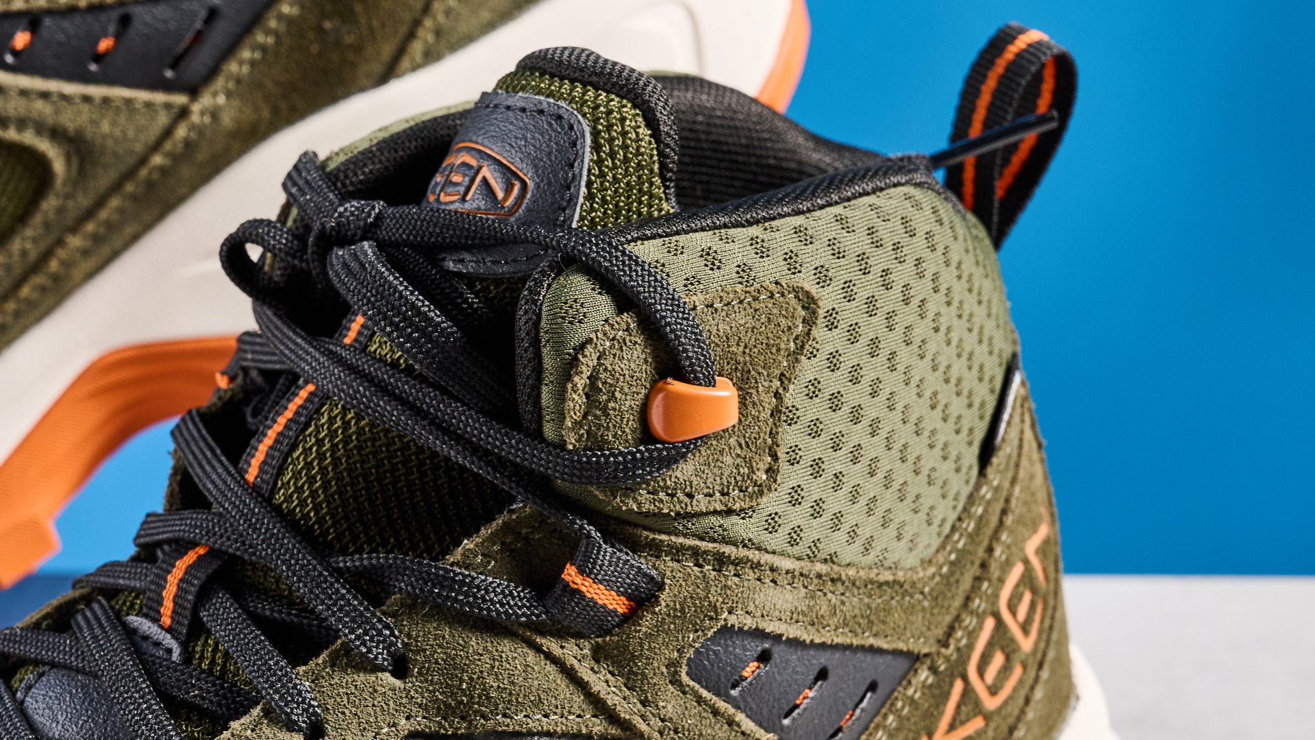 The Keen Hightrail Mid boots in Green on a stone surface against a blue background