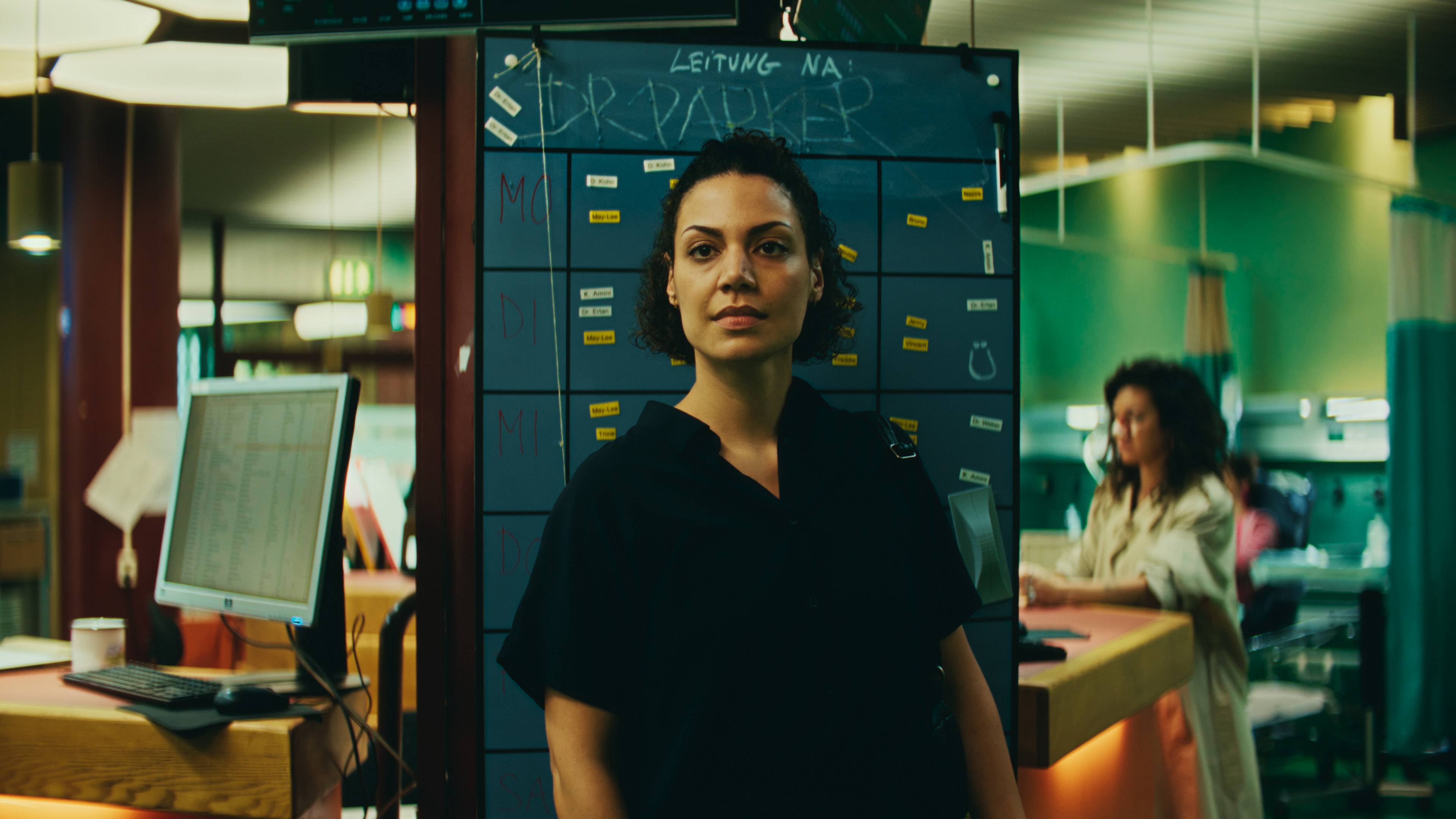 A woman (Haley Louise Jones) stands in front of a board in a hospital emergency room, in 'Berlin ER.'