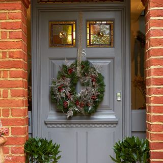 A grey wooden front door decorated with a Christmas wreath hung on a glittery ribbon