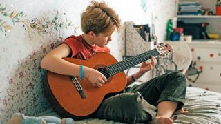 Child plays acoustic guitar in their bedroom
